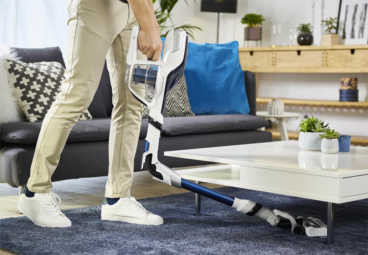 Hombre aspirando debajo de una mesa blanca